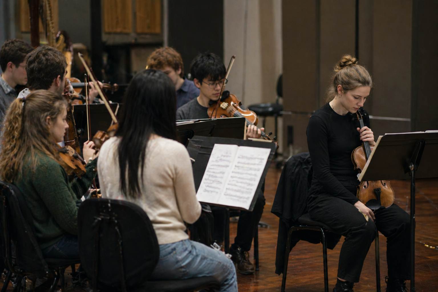 String section seated in rehearsal with one player slightly apart and looking down at the stand