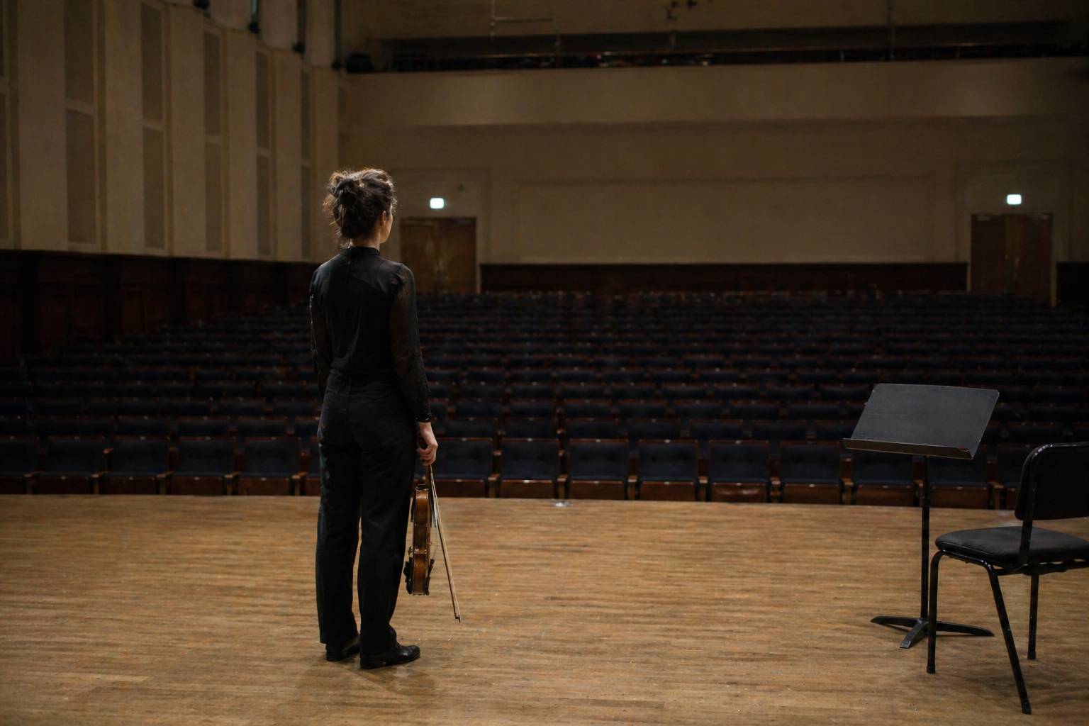 Musician standing alone on stage in an empty hall, taking a calm breath before playing