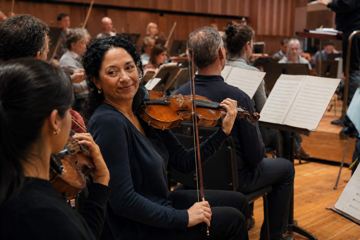 Violinist in orchestra rehearsal turning to a colleague with a relaxed expression while playing Violinist in orchestra rehearsal turning to a colleague with a relaxed expression while playing