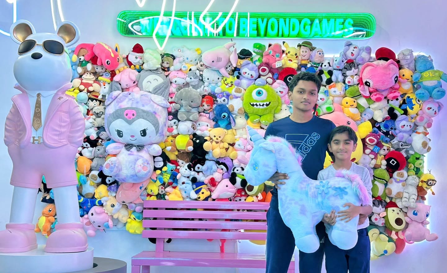Boys with a unicorn plush under the Welcome to Beyond Games neon sign