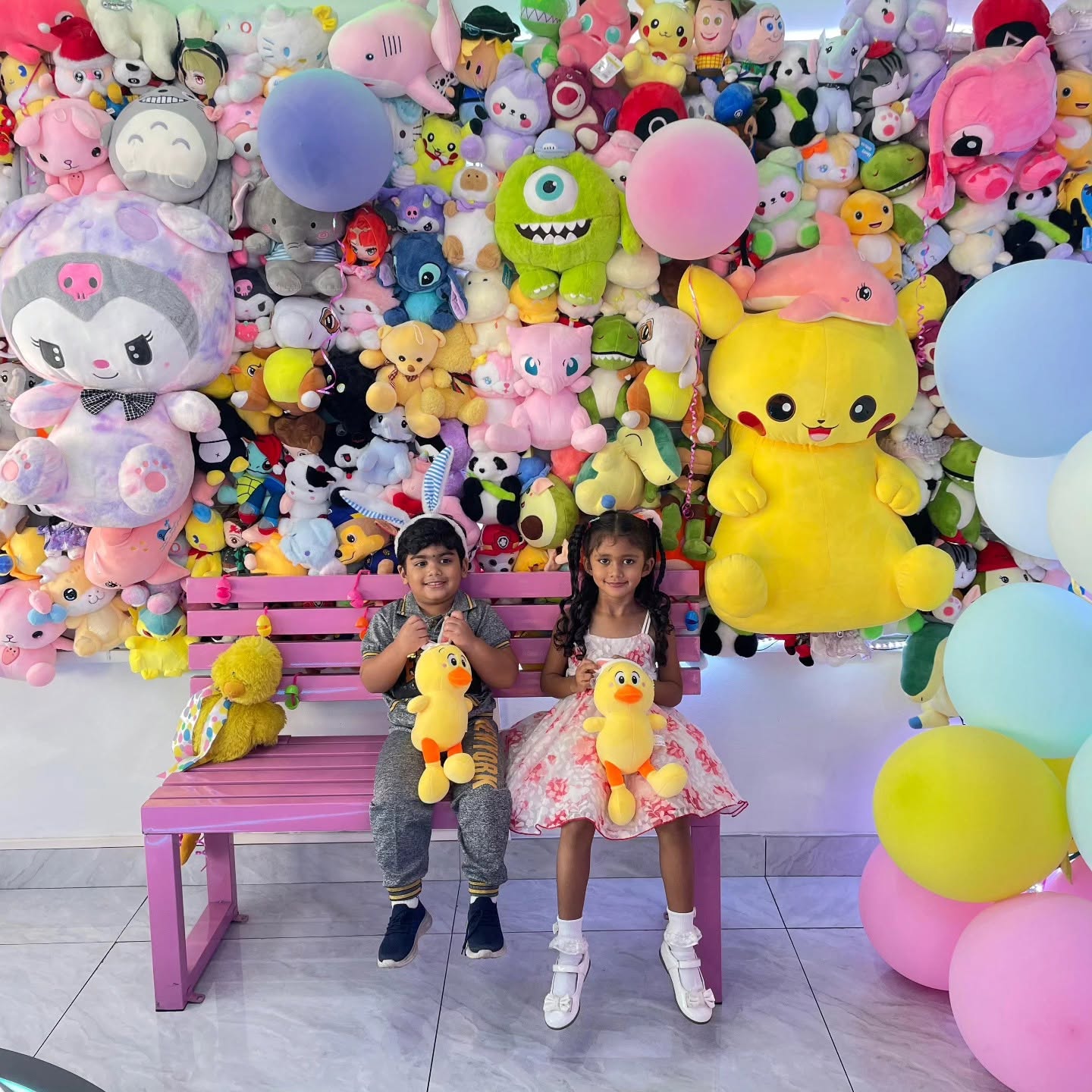 Kids on a bench in front of the plushie prize wall