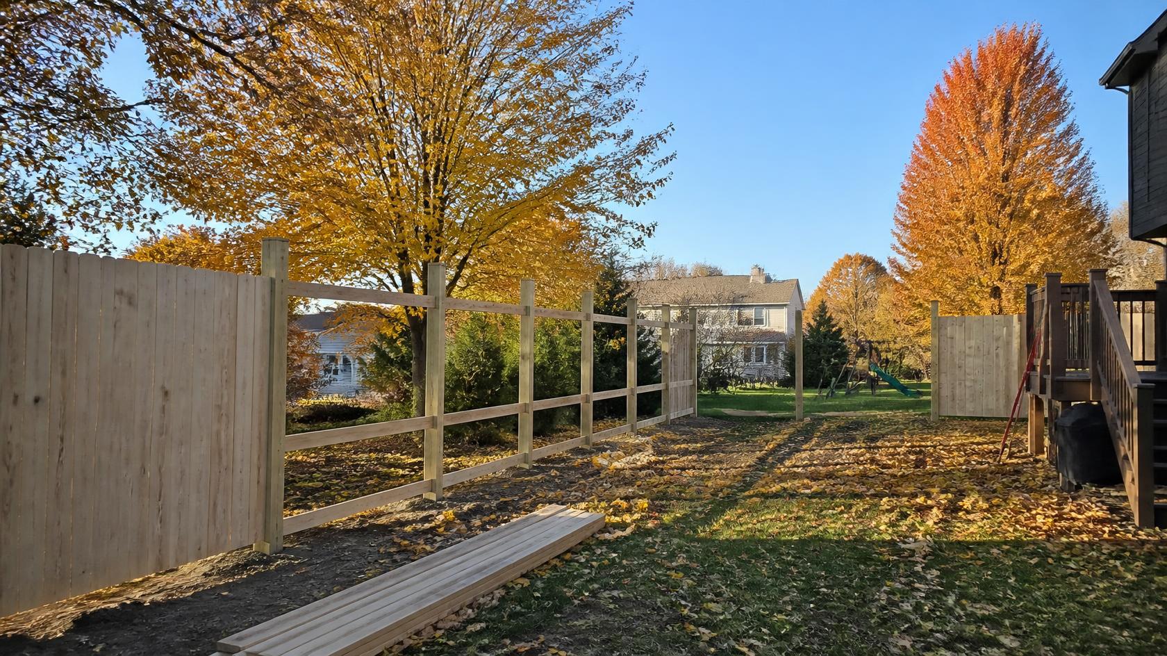 Fence contractor preparing a residential yard in Genoa, IL for fall fence installation, measuring the property line and marking post locations.