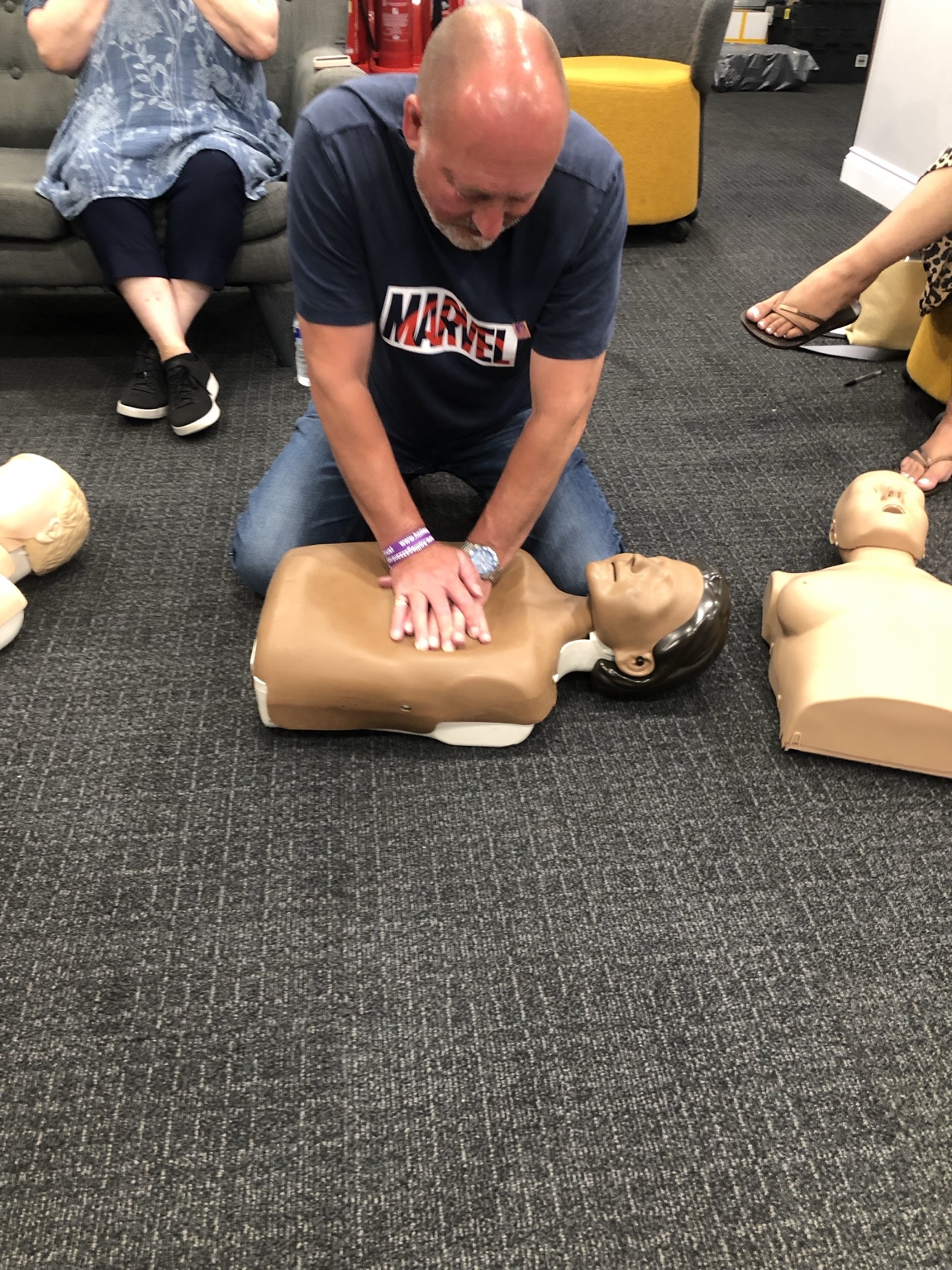 A learner practising adult CPR on a training manikin on the floor