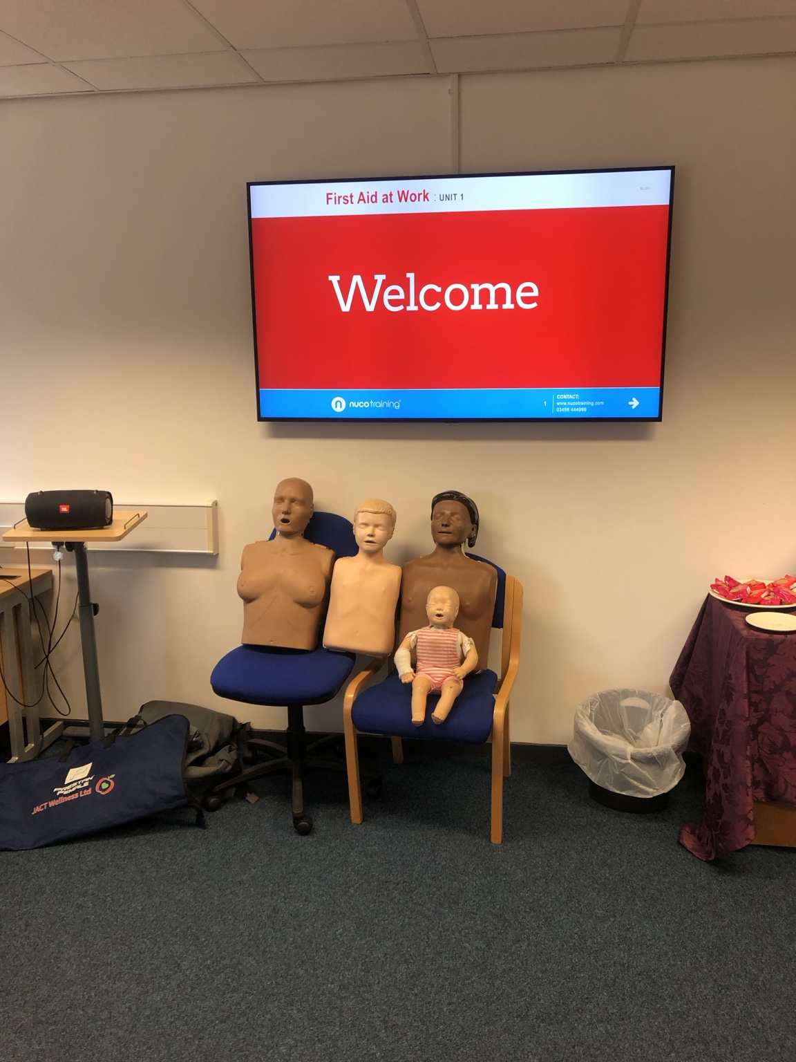 First aid training equipment set out for a First Aid at Work course, with adult, child and baby training manikins and a Nuco training welcome screen