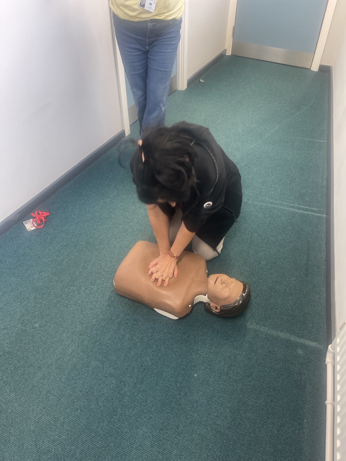 A learner practising CPR on a training manikin on the floor during a First Aid at Work course