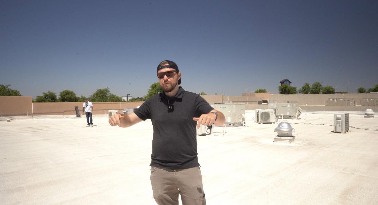 Joa Barron standing on a bright commercial roof pointing at the deck
