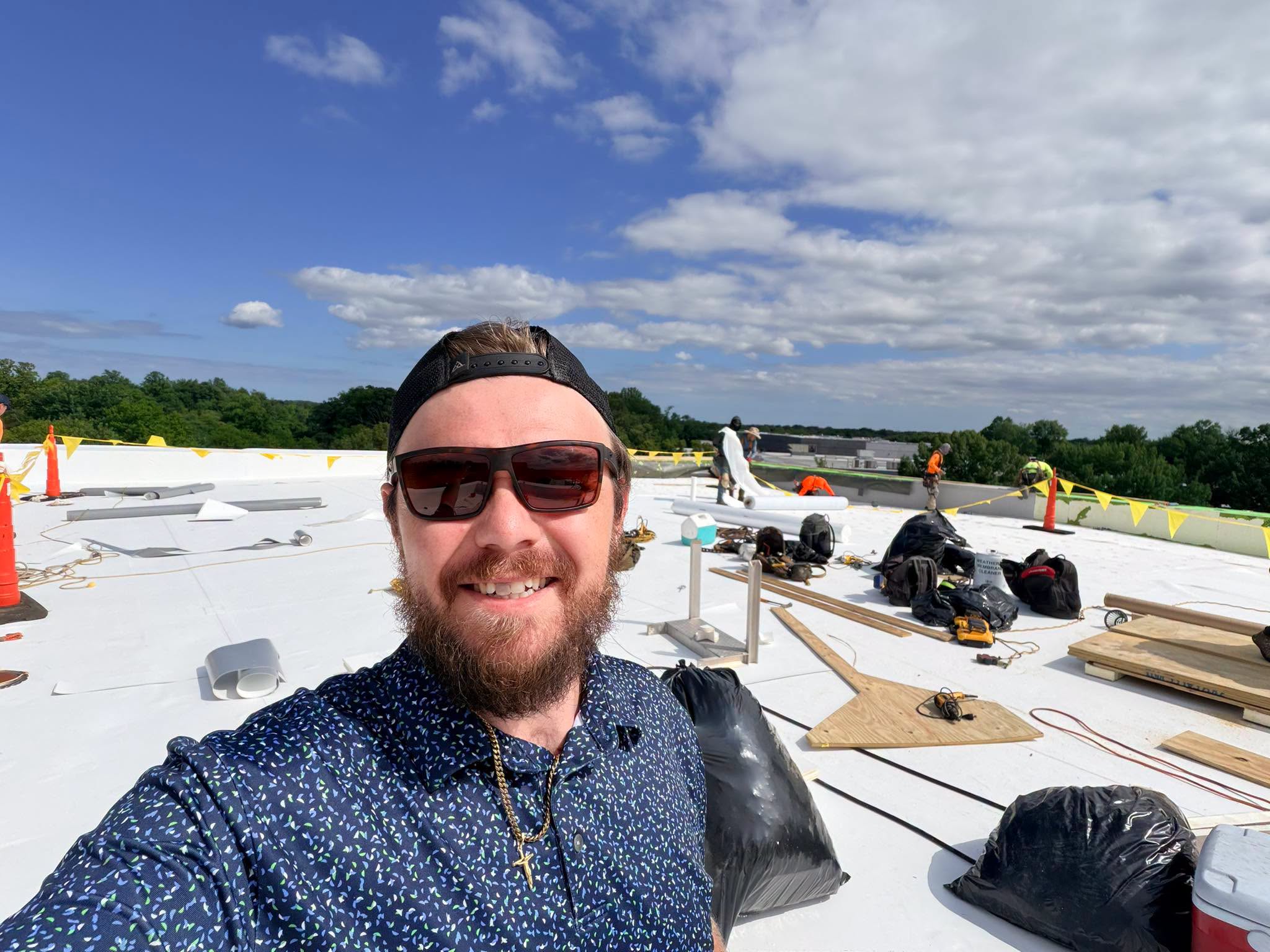 Joa Barron, QURI founder, on a commercial roof with a crew working behind him