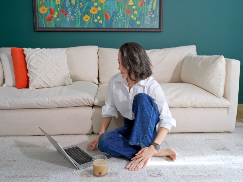 Alex sitting on floor with legs crossed working on laptop with coffee