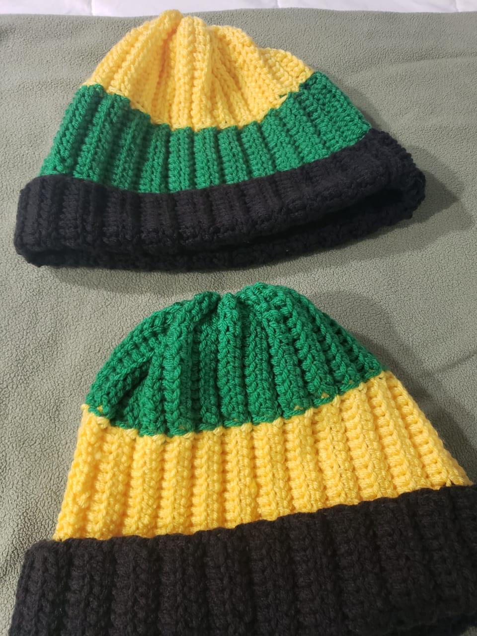Two ribbed crochet beanies in black, green and gold stripes — one with a gold top, one with a green top
