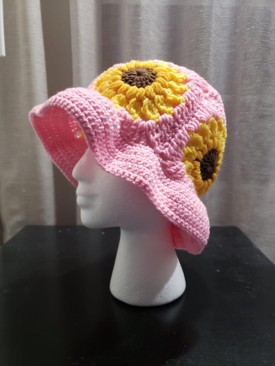 Pink crochet bucket hat with yellow sunflower squares and a wavy brim, shown on a mannequin head