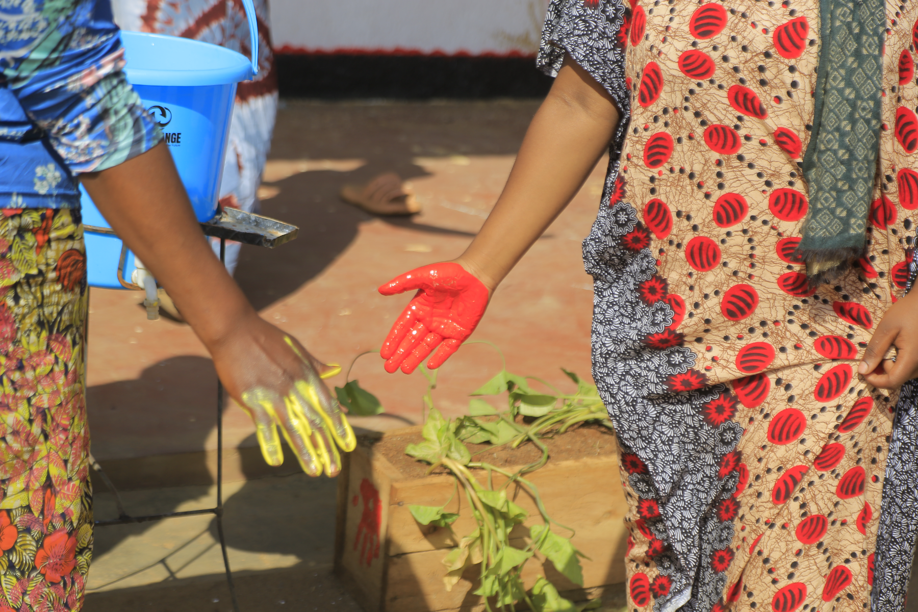 Two women hold up hands covered in yellow and red paint