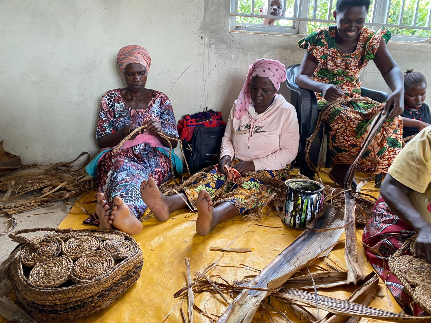 Women sit together weaving banana bark into baskets