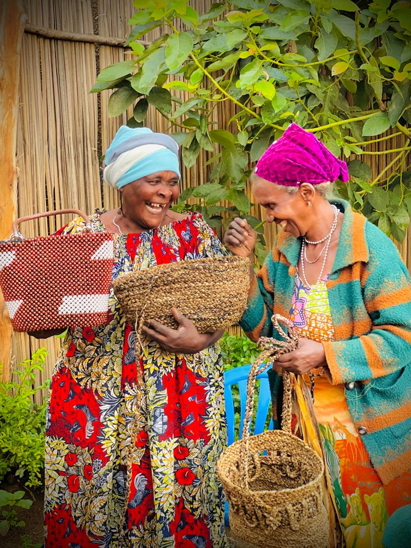 Two women laugh together as they show their woven baskets