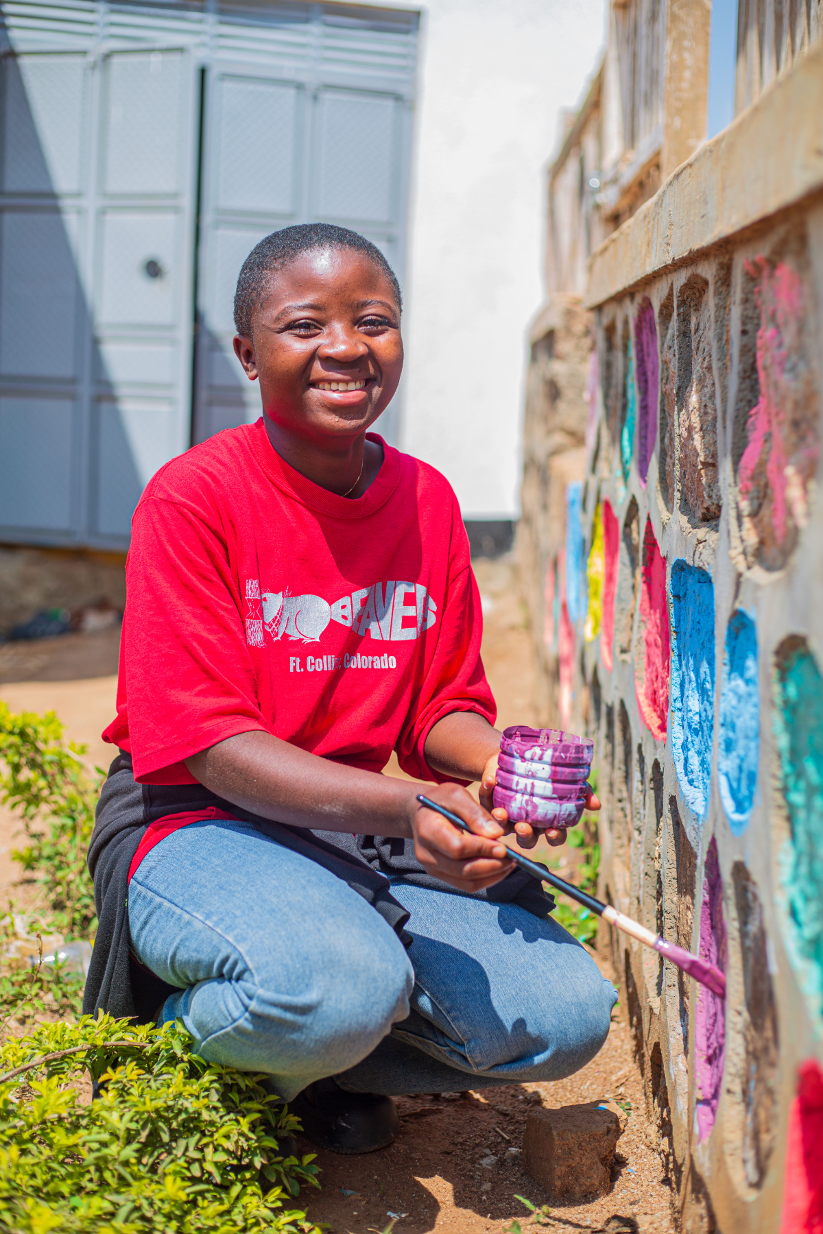 A smiling young woman paints colorful stones on a wall