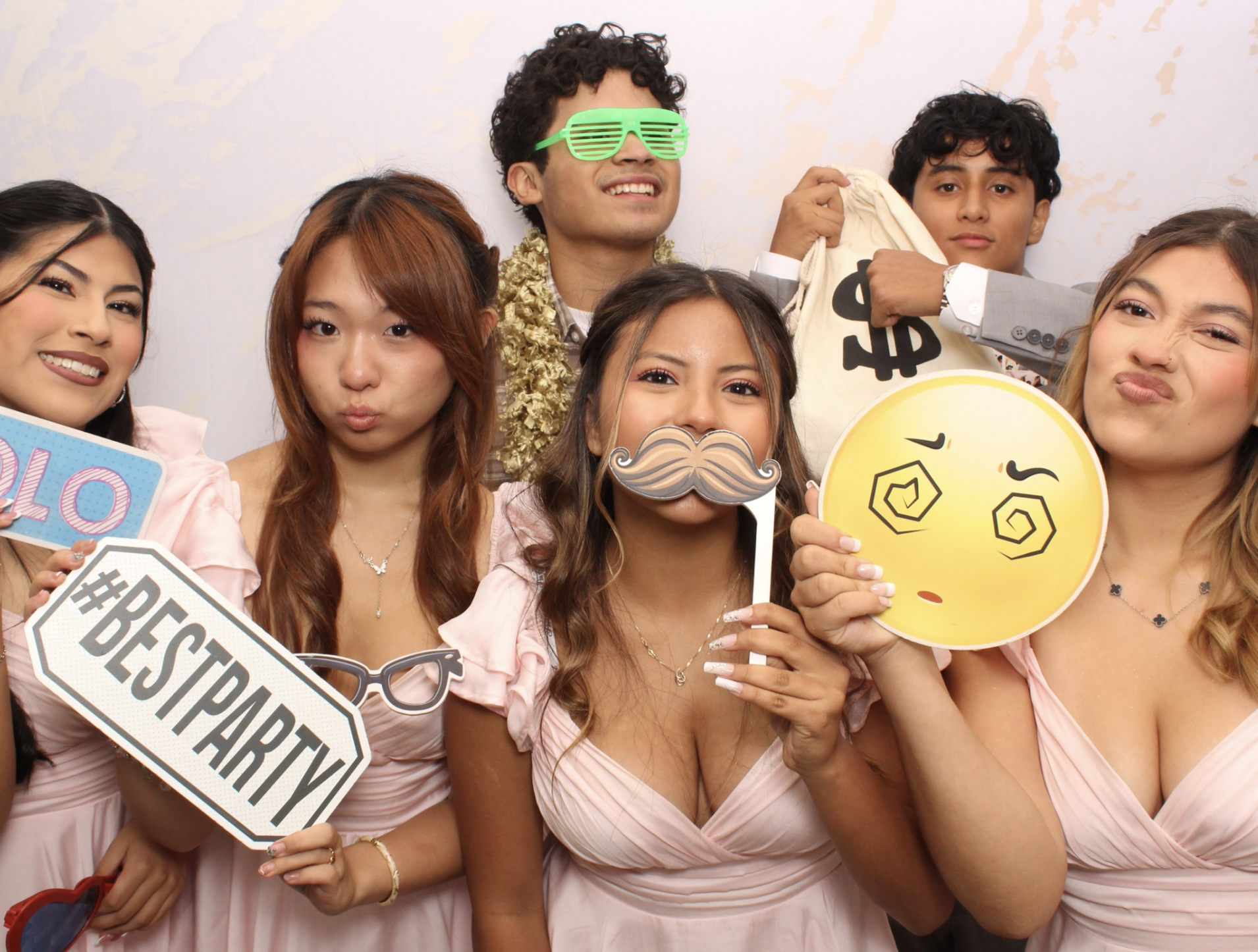 Quinceañera guests posing with colorful glasses and signs against a gold-and-white marble photo booth backdrop