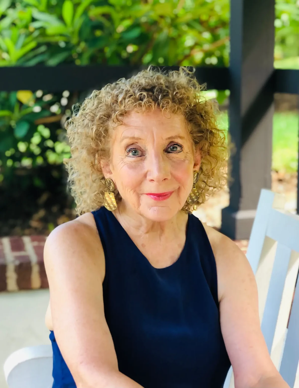 Portrait of poet and novelist Sandra B. Dreis seated outdoors in a navy dress.