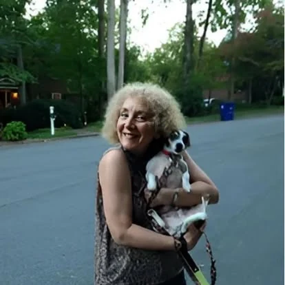 Sandra B. Dreis smiling outdoors while holding a small dog.