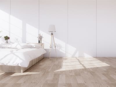 Bright and airy bedroom with minimalistic decor, featuring a low-profile bed, light wood flooring, and a tall floor lamp, emphasizing simplicity and natural light.