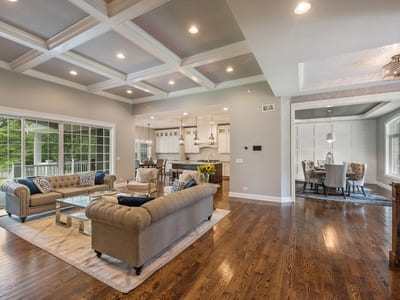 Spacious open-concept living area with coffered ceilings, hardwood floors, and elegant furniture, connecting to a modern kitchen and dining room.