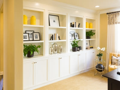 Built-in white cabinets with open shelving, decorated with yellow accents, plants, and framed photos, creating a cozy and organized living space.