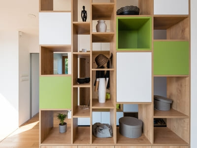 Contemporary wooden shelving unit with green and white cubbies, showcasing a mix of decorative items, storage boxes, and plants.