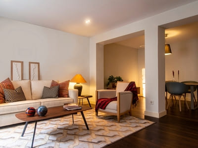 Cozy living room with a neutral-toned sofa, wooden coffee table, patterned rug, and warm lighting, creating a welcoming and comfortable space adjacent to the dining area.