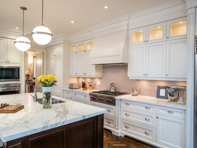 Luxurious kitchen featuring white cabinetry, marble countertops, and stainless steel appliances, illuminated by elegant pendant lighting.