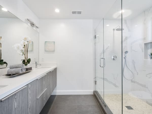 Minimalist bathroom with a glass-enclosed shower, gray tiled floor, white walls, and a long vanity with a modern sink, emphasizing a clean and contemporary design.