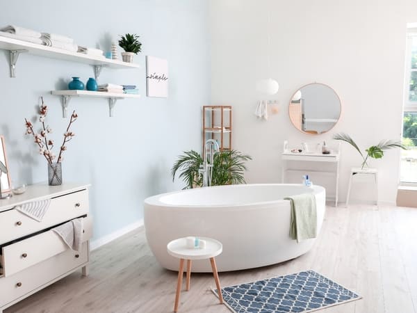 Bright and airy bathroom featuring a freestanding bathtub, light blue walls, white furniture, and stylish decor, creating a relaxing and serene environment.