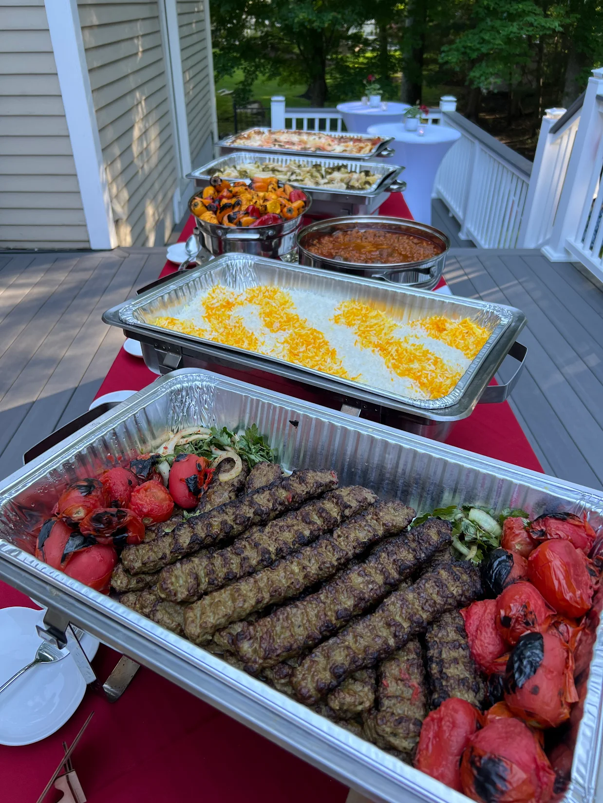 A full Chop Kabob catering spread — trays of beef koobideh, saffron rice, grilled vegetables and Persian stew set up at a customer's outdoor event