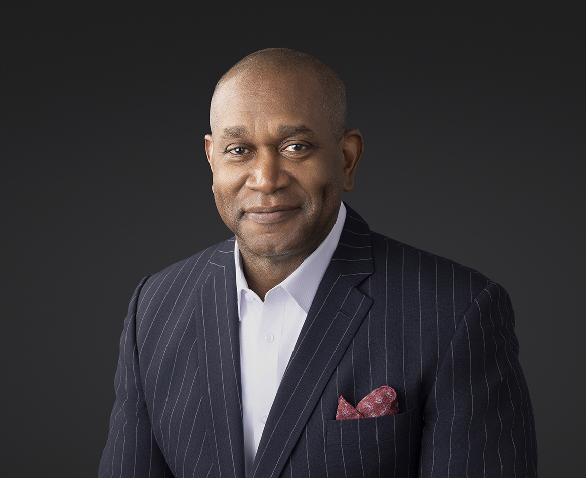 Man in a dark pinstripe blazer and pale shirt against a dark studio background. Man in a dark pinstripe blazer and pale shirt against a dark studio background.