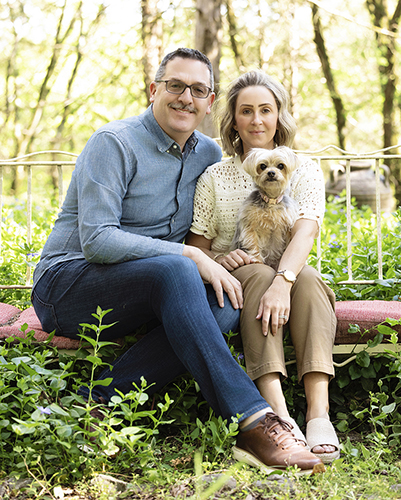 Couple seated outdoors holding a small light-colored dog