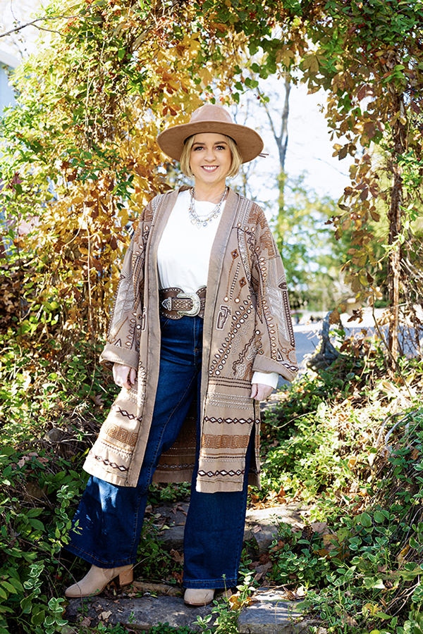 Angie Joseph outdoors in a brimmed hat, white top, jeans, and a patterned wrap.