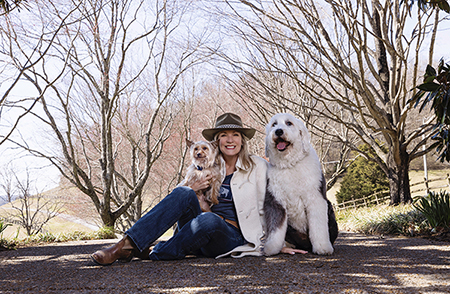 Woman in a hat sitting with two dogs on a wooded footbridge