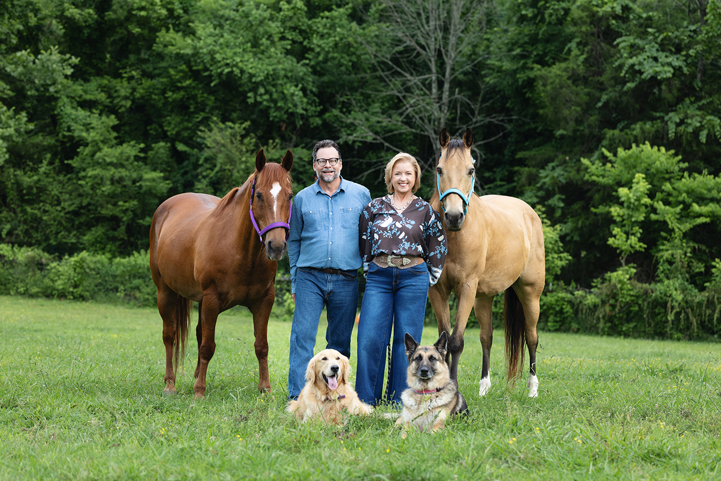 Angie Joseph and a man standing outdoors between two horses, with a dog at their feet.