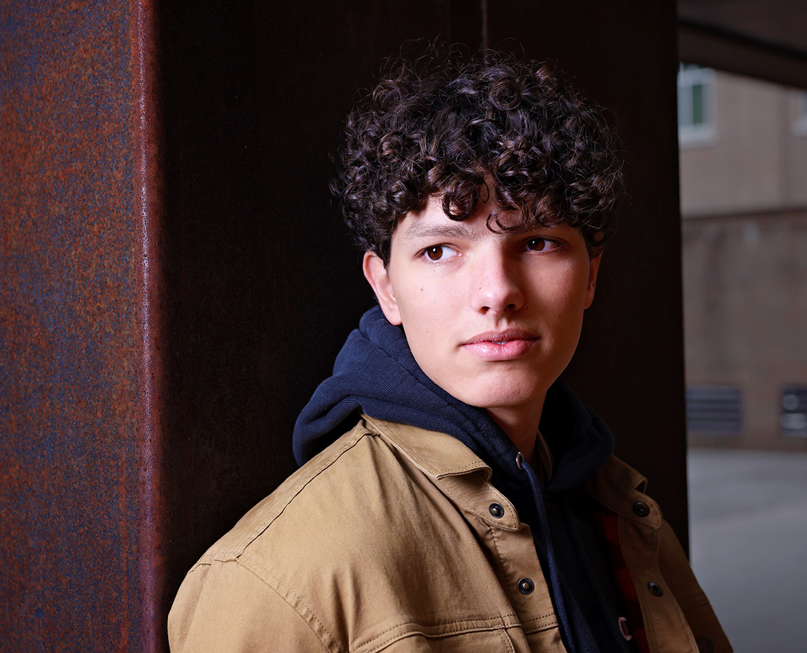 Senior boy with curly hair wearing a jacket against a dark background. Senior boy with curly hair wearing a jacket against a dark background.