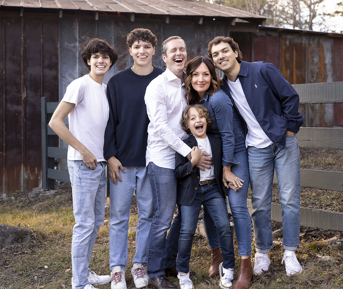 Parents and their four sons smiling together beside a wooden fence. Parents and their four sons smiling together beside a wooden fence.