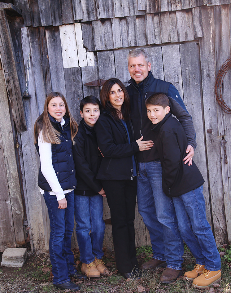 Williams family standing close together against a rustic wooden wall. Williams family standing close together against a rustic wooden wall.