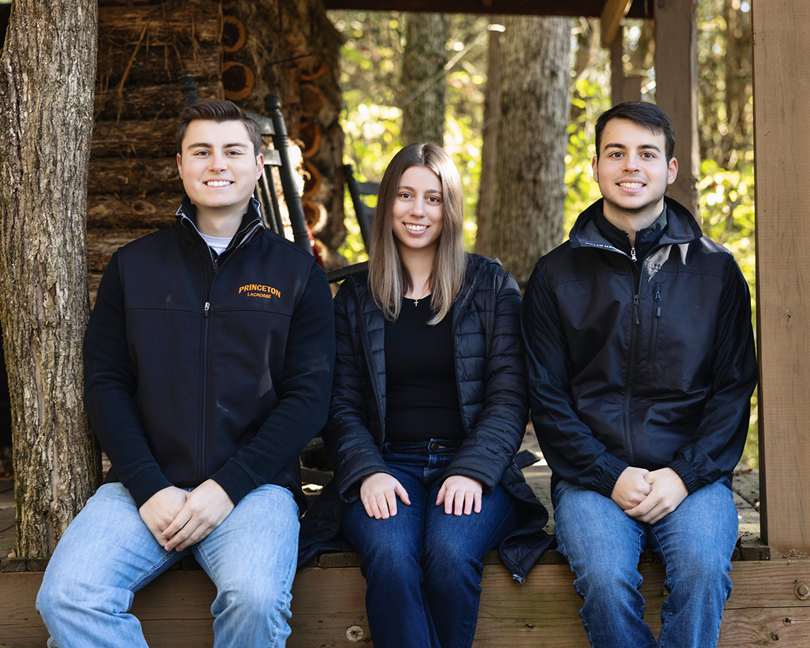Three Williams siblings seated together outdoors in dark jackets. Three Williams siblings seated together outdoors in dark jackets.