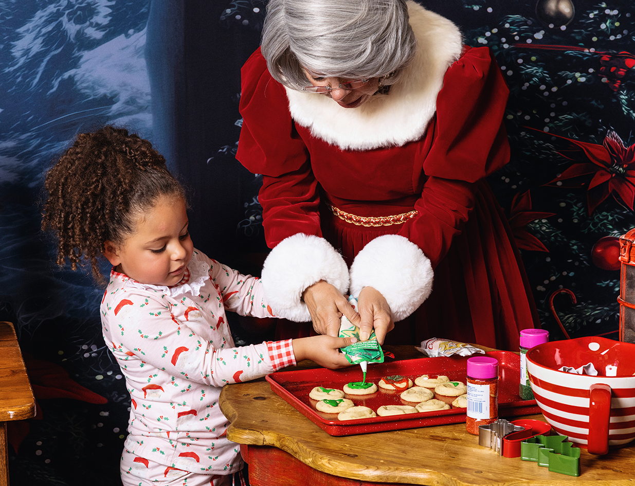 Mrs. Claus helps a young girl decorate cookies at the Christmas cookie station.