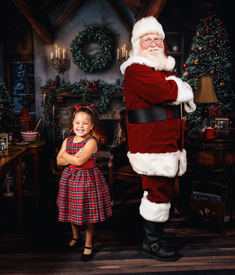 Smiling young girl and Santa standing back to back with folded arms in the Christmas studio.