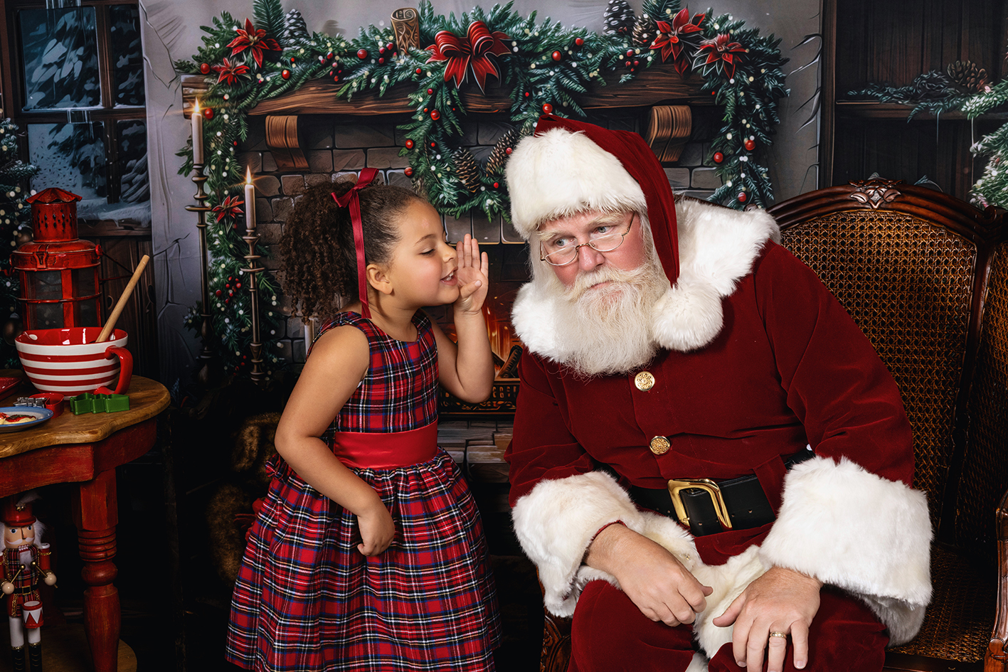Young girl in a plaid Christmas dress whispering to Santa beside the fireplace.
