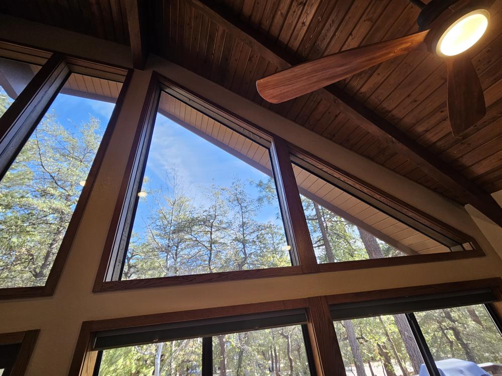 Custom solar screens on tall gable windows, seen from inside looking up at the pines