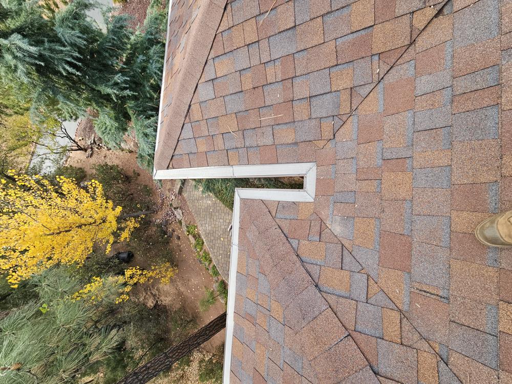 Gutter guard wrapping a stepped roof corner among fall colors