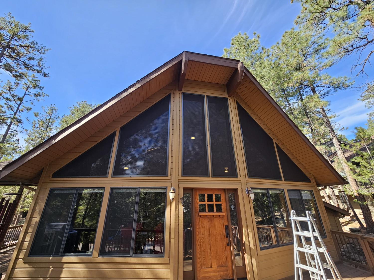 A-frame cabin with custom solar screens on its gable windows among the pines