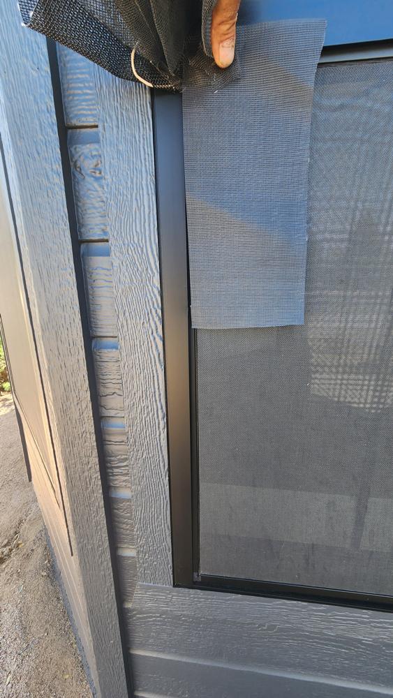 Technician's hand holding a mesh sample against a customer's screen to match it