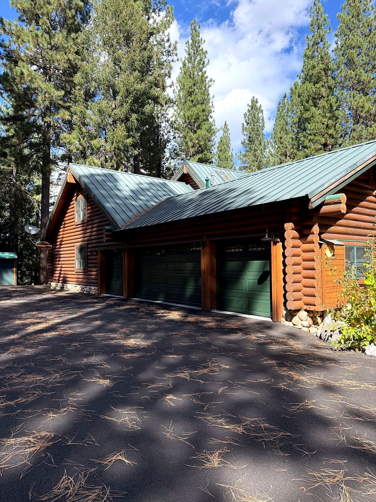 Freshly stained log home with a green metal roof, restored by DBT Construction