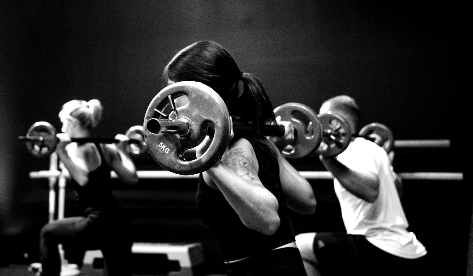 Three athletes training side by side with barbells