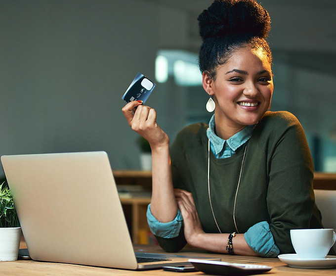 A woman smiling at her desk, holding a credit card beside an open laptop