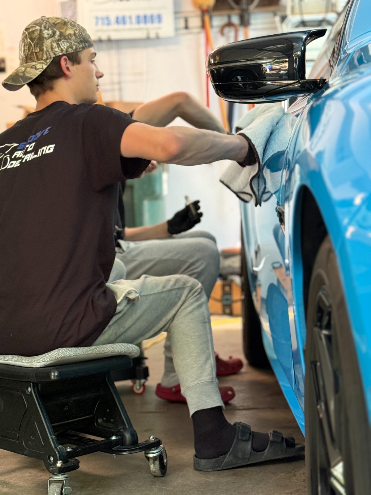 Two Smoove detailers in branded shirts hand-detailing a blue BMW M8 — mobile detailing team Eau Claire